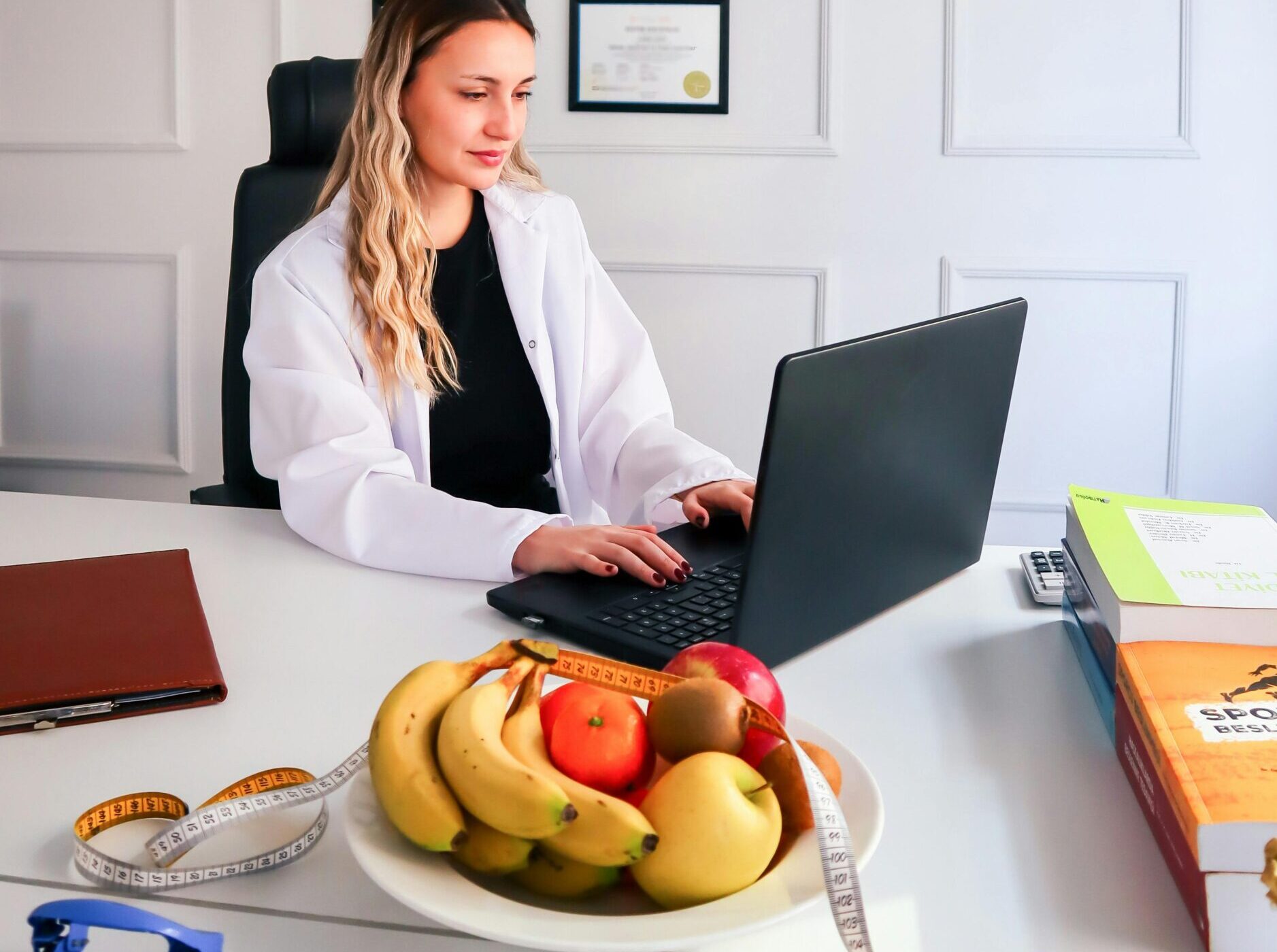 Nutritionist working at desk with laptop and healthy fruits in office setting.